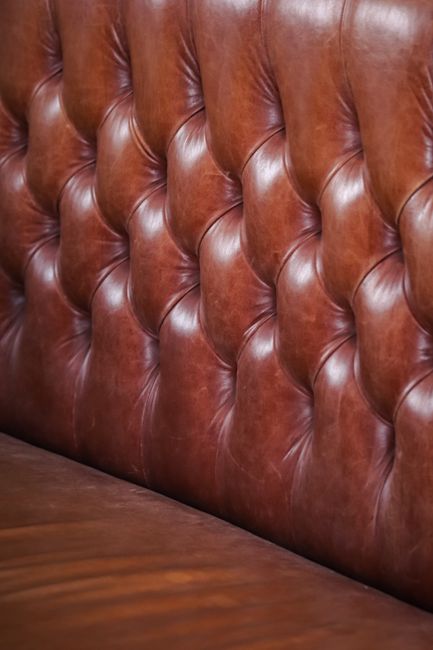 Close-up of a plush, deep blue velvet sofa with tufted upholstery, showing well-maintained, clean, and smooth surfaces with visible stitching and button-tufting details. The sofa is situated in a soft